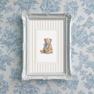 May include: A framed print featuring a watercolor illustration of a teddy bear with a blue bow. The print is set against a striped background within a white ornate frame. The background is a blue floral wallpaper.