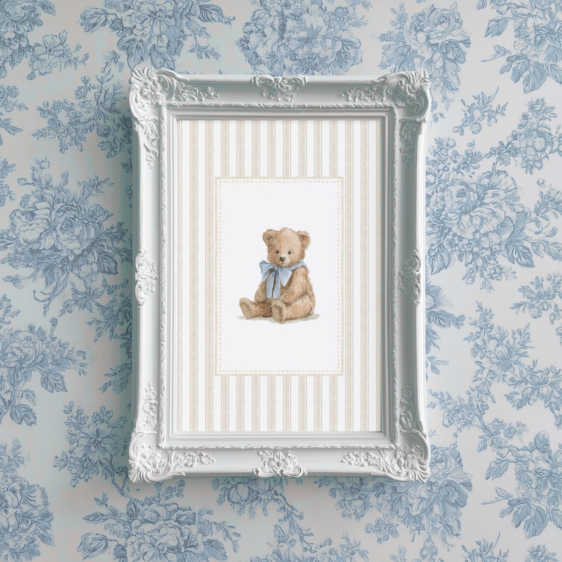 May include: A framed print featuring a watercolor illustration of a teddy bear with a blue bow. The print is set against a striped background within a white ornate frame. The background is a blue floral wallpaper.