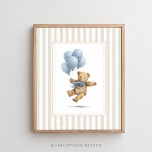 K&ouml;nnte beinhalten: Ein gerahmter Druck mit einer Aquarellillustration eines Teddyb&auml;ren, der mit blauen Luftballons schwebt. Der B&auml;r hat eine blaue Schleife und befindet sich vor einem wei&szlig;en Hintergrund mit einem gepunkteten Rand. Der Rahmen hat ein Streifenmuster.