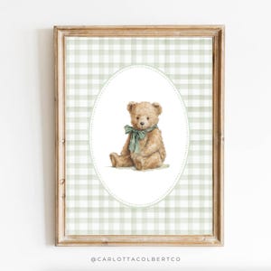 May include: A framed print featuring a watercolor illustration of a teddy bear. The bear is light brown with a green bow, set against a white oval on a green and white gingham background. The frame is a light brown color.