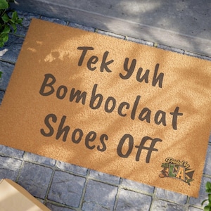 Pode incluir: Um capacho retangular com o texto "Tek Yuh Bomboclaat Shoes Off" em letras marrons escuras. O tapete &eacute; de cor marrom claro e tem uma superf&iacute;cie texturizada. As palavras "Printed by LA" est&atilde;o no canto inferior direito.
