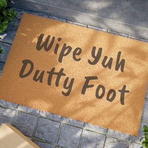Könnte beinhalten: Eine braune Kokosmatte mit dem Text "Wipe yuh Dutty Foot" in schwarzen Buchstaben.