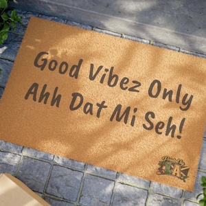 Pode incluir: Um tapete retangular com o texto "Good Vibez Only Ahh Dat Mi Seh!" em letras castanhas escuras. O tapete é de cor castanha clara e assenta numa superfície de pedra cinzenta. O logótipo "Printed by LA" está no canto inferior direito.