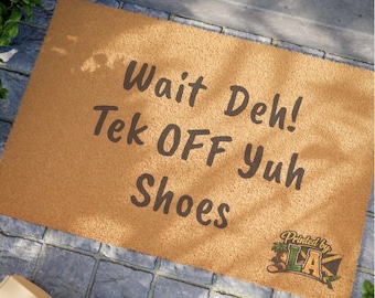 Puede incluir: Una alfombra de puerta rectangular de color marrón claro con el texto "Wait Deh! Tek OFF Yuh Shoes" en marrón oscuro. La alfombra tiene un logotipo en la esquina inferior derecha que dice "Printed by LA".