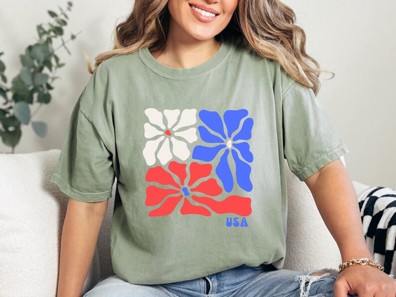 May include: A green t-shirt with a graphic of three stylized flowers in red, white, and blue. The flowers are arranged in a square shape and the word "USA" is printed below them.