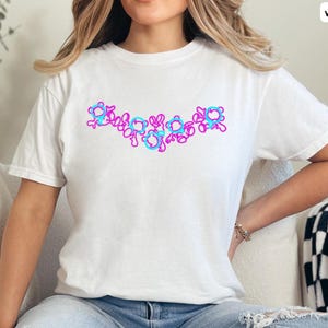 Puede incluir: Una camiseta blanca con un dise&ntilde;o gr&aacute;fico rosa y azul de una serie de c&iacute;rculos conectados.