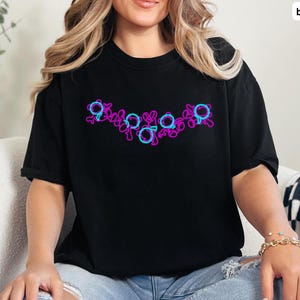 Puede incluir: Una camiseta negra con un dise&ntilde;o gr&aacute;fico rosa y azul de una serie de c&iacute;rculos y espirales.