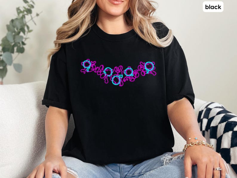 Puede incluir: Una camiseta negra con un dise&ntilde;o gr&aacute;fico rosa y azul de una serie de c&iacute;rculos y espirales.