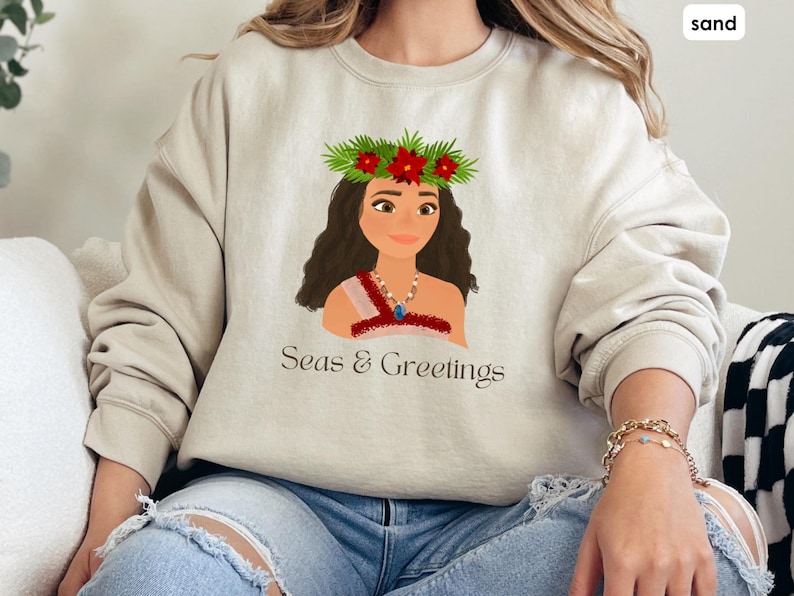 May include: A beige sweatshirt featuring a cartoon illustration of a woman wearing a flower crown and the text "Seas & Greetings".