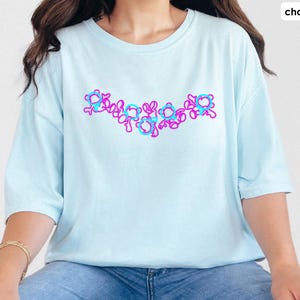Puede incluir: Una camiseta azul claro con un dise&ntilde;o gr&aacute;fico rosa y azul de una serie de c&iacute;rculos conectados. La camiseta est&aacute; hecha de una tela suave y c&oacute;moda.
