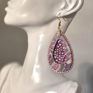 May include: A teardrop-shaped dangle earring featuring a central cluster of pink rhinestones surrounded by a patterned fabric border in shades of pink, blue, and yellow. The edge is lined with small pink beads and it hangs from a gold-tone hook.
