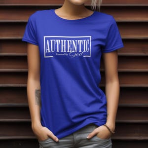 May include: Royal blue t-shirt with the word "AUTHENTIC" in a white rectangular frame. Below the word "AUTHENTIC" is the text "Powered By God" in white script. The shirt has short sleeves and a crew neck.