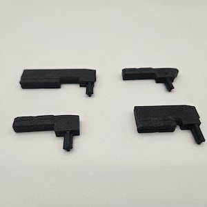 May include: Four small, black, rectangular objects with a right-angle shape and a small, protruding piece. The objects are evenly spaced against a white background. The items appear to be 3D-printed.