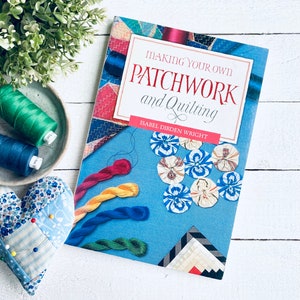 May include: A blue book titled "Making Your Own Patchwork and Quilting" by Isabel Dibden Wright. The cover features colourful patchwork fabric squares, a selection of colourful embroidery floss, and blue and white fabric flowers.
