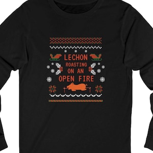 May include: Black long-sleeve shirt with a festive design. The design includes the text "LECHON ROASTING ON AN OPEN FIRE" in white and red, along with images of a pig roasting on a spit, snowflakes, and sleighs.