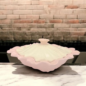 May include: A pink and white ceramic dish with a ruffled edge and a lid. The lid has a flower-shaped knob.