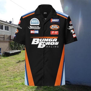 May include: A black short-sleeved button-up shirt with an orange and blue racing design. The shirt features several sponsor logos, including "Buzyn", "True Combo", "Jamokes", "Mogged Technologies", "Bang Xodon", and "Fast Beer". The shirt also has the text "Bunga Bros Racing" in large white letters.