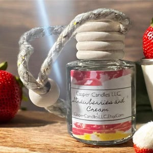 May include: A clear glass bottle with a white lid and a white string hanging from it. The bottle is filled with a clear liquid and has a label that says "Casper Candles LLC Strawberries and Cream CasperCandlesLLC.Etsy.com". There are strawberries in the background.