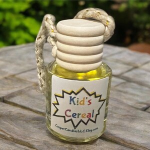 Puede incluir: Una pequeña botella de vidrio transparente con tapa de madera y asa de cuerda trenzada. La botella contiene un líquido amarillo y una etiqueta que dice "Kid's Cereal" en un diseño de estrella colorido. También es visible el nombre de la tienda Etsy.