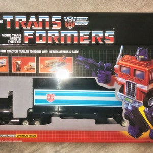 Pode incluir: Um brinquedo vintage Optimus Prime dos Transformers em sua embalagem original. A caixa apresenta o texto "The Transformers" e "More Than Meets The Eye!". O brinquedo é um caminhão vermelho, azul e preto que se transforma em um robô.