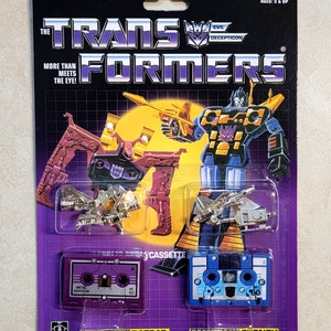 Puede incluir: Un empaque de juguete vintage de Transformers con los Decepticons Ratbat y Frenzy. El empaque es morado y negro con una figura de robot plateada y dorada en el centro. El empaque incluye dos cintas de cassette, una morada y una azul, con el texto "Metal Position" y "MC 60" en ellas.