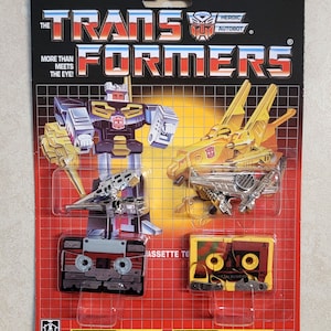 May include: Vintage Transformers toy packaging featuring the Autobot Steeljaw. The packaging is red, yellow and black with a grid pattern. The toy is a yellow and silver robot that transforms into a cassette tape. The packaging includes the text "Autobot Steeljaw" and "5934/5724. Asst."