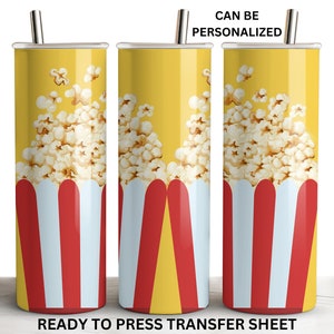 May include: A ready to press sublimation transfer sheet featuring a design of a yellow tumbler with a red and white striped popcorn bucket filled with popcorn. The text "CAN BE PERSONALIZED" is at the top of the image.