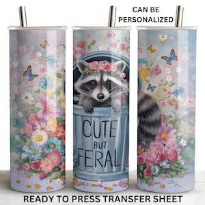 May include: A sublimation design featuring a raccoon with a floral background and the text "Cute But Feral". The design is ready to be pressed onto a tumbler.