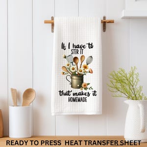 May include: White kitchen towel with the text "If I have to stir it that makes it homemade." The towel features a graphic of kitchen utensils and flowers in a metal pitcher. The towel is hanging on a wooden rod.