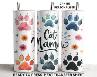 May include: White tumbler with a paw print design in pink, blue, and black. The tumbler has a silver straw and the text "Cat Name" in black script. Floral and heart accents are scattered around the paw prints. The text "CAN BE PERSONALIZED" is at the top.