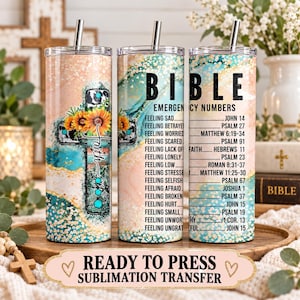 May include: Three cylindrical tumblers with metal straws featuring a peach and teal marble background. One tumbler displays a cross with sunflowers and the word faith. Two tumblers feature the text BIBLE EMERGENCY NUMBERS with a list of feelings and corresponding scripture references.