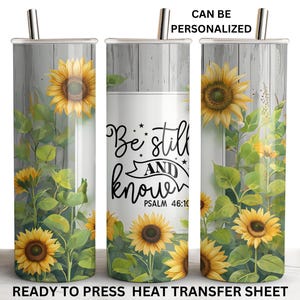 May include: A white tumbler with a woodgrain background and a sunflower design. The tumbler has a quote that reads "Be still and know" with the scripture reference "Psalm 46:10".