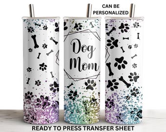 Könnte beinhalten: Ein weißer Becher mit einem schwarz-weißen Pfotenabdruck- und Knochenmuster. Der Becher hat einen Regenbogen-Glitzer-Effekt am Boden. Der Text "Dog Mom" befindet sich in einem schwarzen quadratischen Rahmen auf dem Becher. Der Becher ist bereit, mit einer Transferfolie bedruckt zu werden.