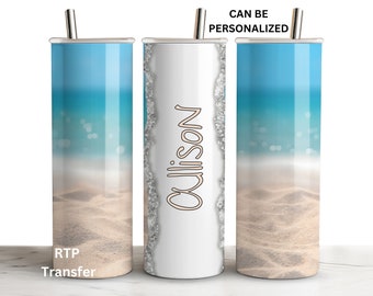 May include: Three stainless steel tumblers with a beach scene design. The tumbler on the left has a blue ocean and sand beach. The tumbler in the middle is white with the name "Allison" in pink script. The tumbler on the right has a blue ocean and sand beach. The text "CAN BE PERSONALIZED" is above the tumblers.