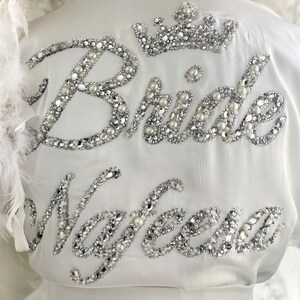May include: White satin robe with a silver and white beaded design that says 'Bride' and 'Nayeema'.