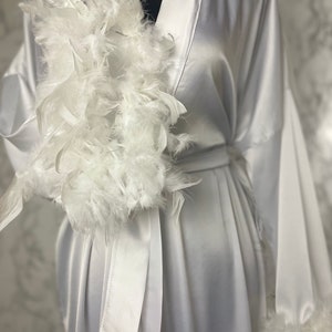 May include: A white satin robe with a white feather trim around the neckline and cuffs. The robe has a sash tie at the waist.