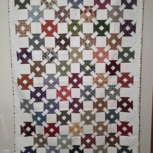 May include: A rectangular quilt featuring a repeating pattern of multi-colored fabric squares in various prints and solid colors, interconnected by a white lattice grid. The quilt displays a diverse palette including red, blue, green, and brown.