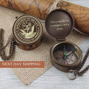 May include: A brass compass with a chain and a lid that has the Department of the Navy seal and the text "Live your life by a compass, not a clock."