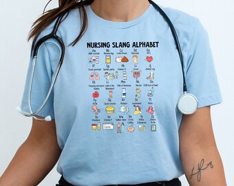 May include: A light blue t-shirt with a graphic of a nursing slang alphabet. The graphic features icons and text representing common nursing terms and abbreviations. The shirt is worn by a person with a stethoscope around their neck.