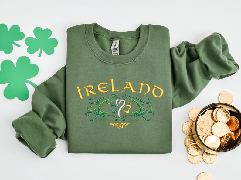 K&ouml;nnte beinhalten: Gr&uuml;nes Sweatshirt mit dem Wort "IRELAND" in goldener Schrift und einem Kleeblatt-Design bestickt.