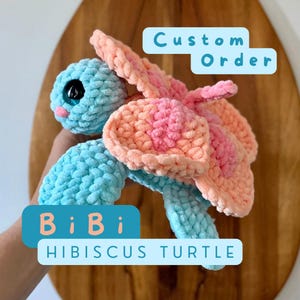 May include: A crocheted turtle toy with a pink and orange hibiscus flower shell. The turtle is light blue and has large, black eyes. The text "Custom Order" and "BiBi Hibiscus Turtle" is visible in the image.
