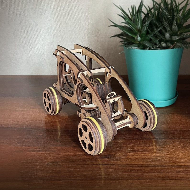 May include: A wooden toy car with yellow wheels and intricate gears visible. The car is made of natural wood and has a detailed design.