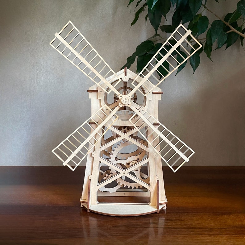May include: A wooden model of a windmill with intricate gears and blades. The windmill is made of light wood and has a natural finish.
