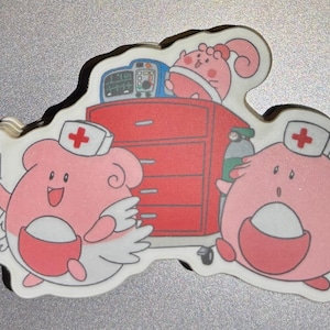 May include: A sticker featuring cartoon characters in a medical setting. Two pink, egg-shaped characters wearing nurse hats with red crosses are present. A red medical cabinet and medical equipment are also depicted.