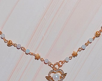 May include: A delicate gold necklace with a heart pendant featuring a pearl and wings. The necklace is adorned with small gold hearts and white pearls.