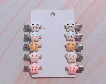 May include: A set of eight star-shaped hair clips with different animal faces. The clips are silver with white, pink, brown, and blue accents.