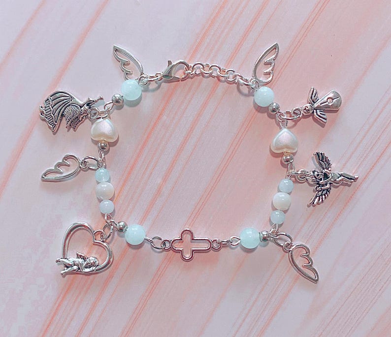 May include: A silver charm bracelet with a variety of angel and heart charms, as well as light blue and white beads.