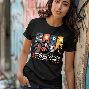 Könnte beinhalten: Schwarzes T-Shirt mit einer farbenfrohen Grafik von Horrorfilmfiguren, darunter Freddy Krueger, eine Kürbiskopffigur, Pennywise der Clown und eine Silhouette. Der Text "The Boys of Fall" befindet sich darunter.