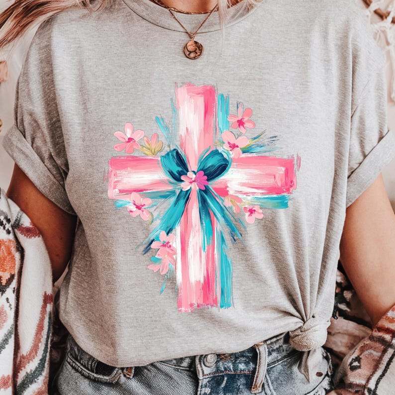 Puede incluir: Una camiseta gris con un dise&ntilde;o de cruz pintada en rosa y azul. La cruz est&aacute; rodeada de flores rosas y azules.