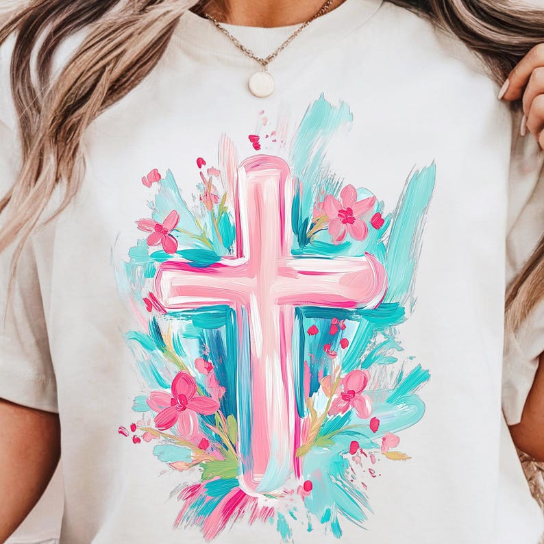 May include: A white t-shirt featuring a pink cross surrounded by blue and pink flowers. The cross is painted in a brushstroke style.